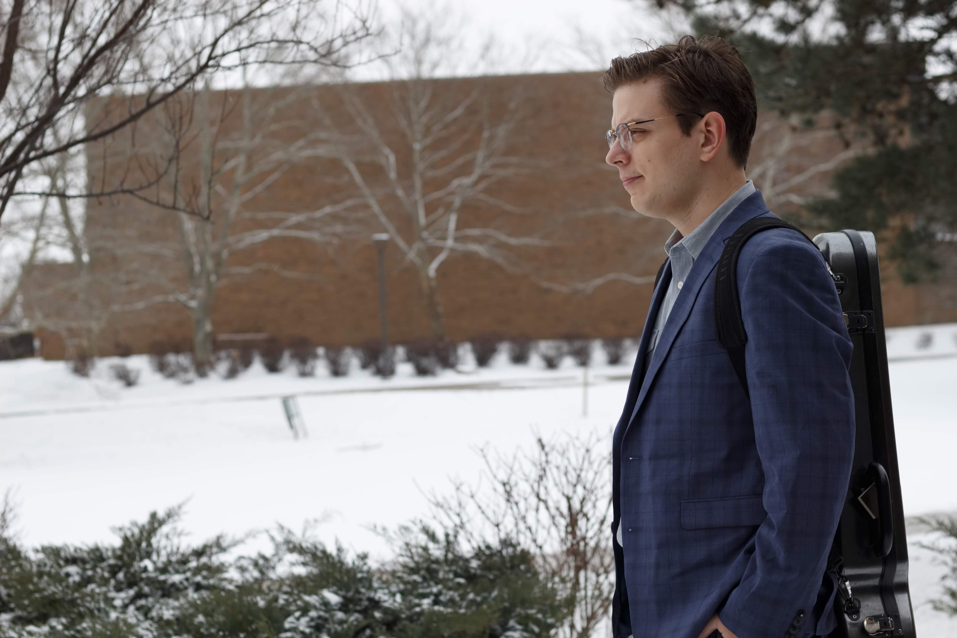 Dr. Alex Malaimare walking across the Marshall University campus with his violin case